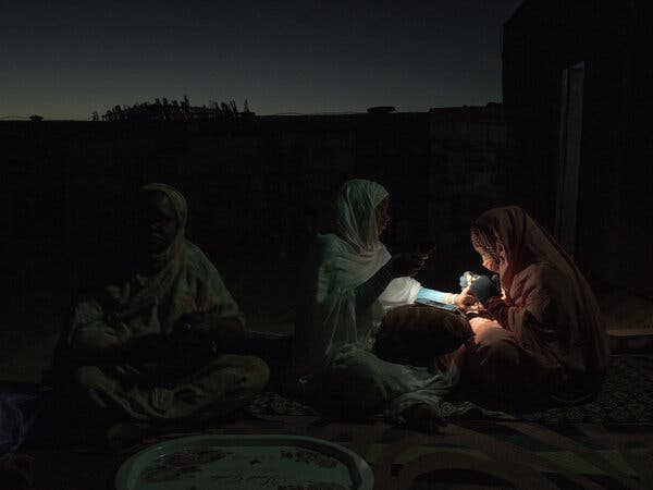 Three people sit in darkness, with a small light illuminating the space between two of them.