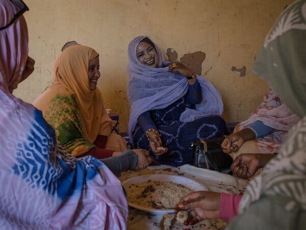 Women smile and talk as they sit around a bowl of food.