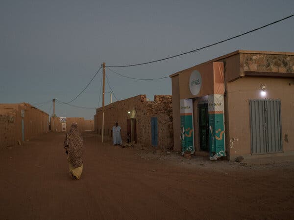 A woman walks along a street in a desert region town.