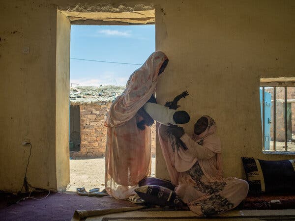 A woman hands her young child to another woman at the entrance to a home.