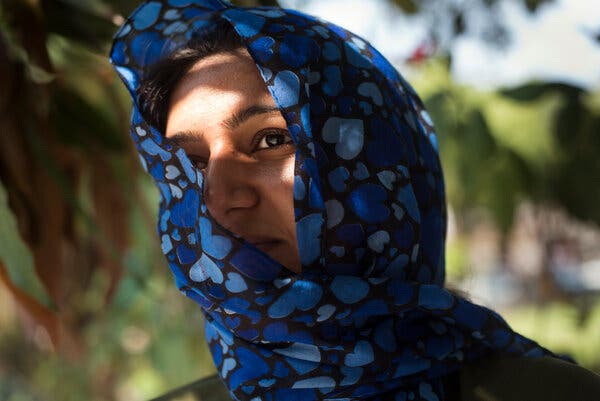 A portrait of a woman, her face partly covered by a scarf with blue hearts on it.