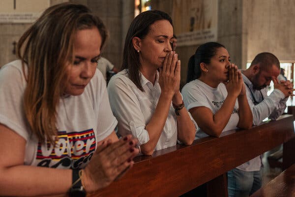 Ms. Machado, wearing a white button down shirt, kneels in prayer.