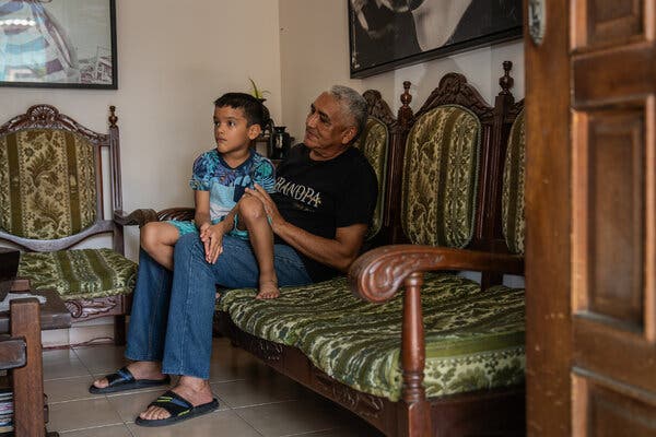 A man holds a young boy while seated on a couch.