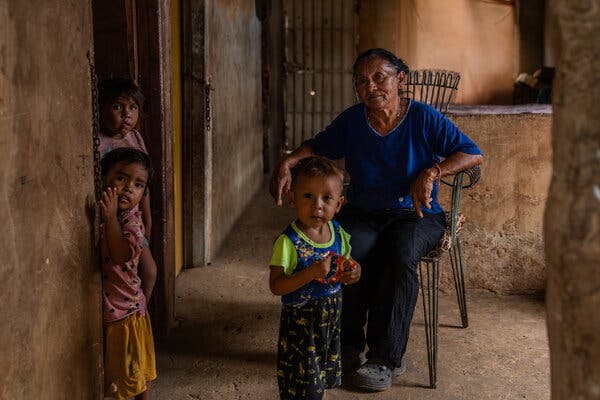 A woman sits in a chair with three children nearby.